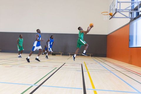 African american basketball player leaping for layup in indoor gymnasium during game