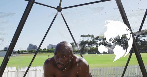 Bare-chested mature athlete training under triangular metal frame on urban sports field