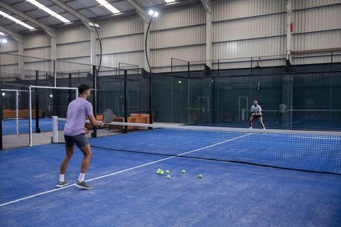 Indoor padel players engaging in dynamic rally and training on blue court with rackets