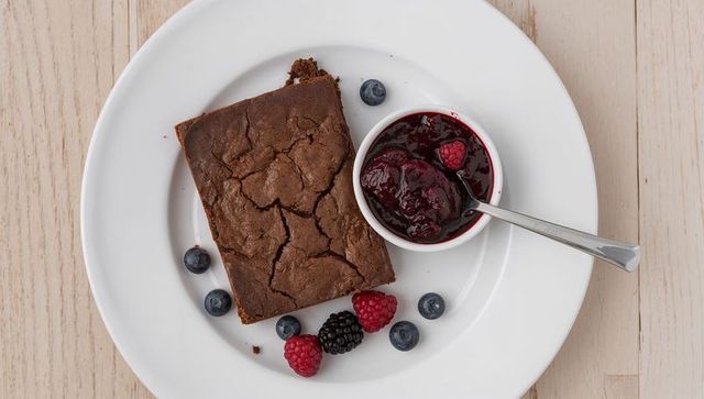 Decadent chocolate brownie sitting with mixed berry compote on white plate overhead view