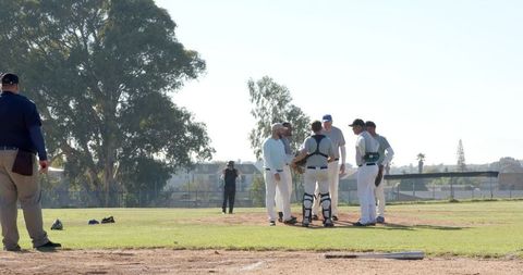 Baseball players huddling on pitcher's mound during sunny game, catcher wearing gear