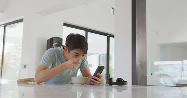 Young Man Eating Breakfast While Using Smartphone in Modern Kitchen - Download Free Stock Images Pikwizard.com