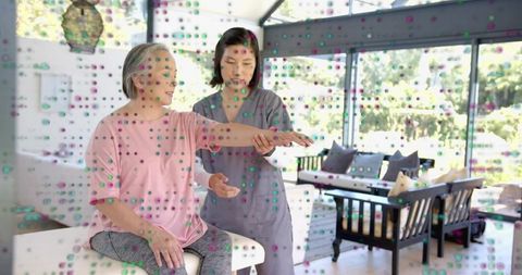 Home caregiver guiding senior woman through arm mobility exercise in bright living room