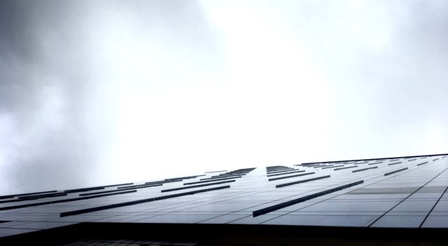 This image features an upward view of a modern skyscraper with a glass facade, set against a cloudy sky. The visually striking perspective highlights the building's height and architectural details. Ideal for use in articles, presentations, or websites related to architecture, urban life, or modern infrastructure.
