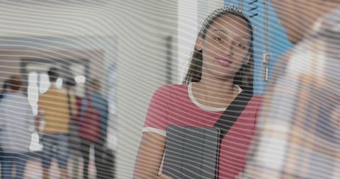 High school student leaning by lockers holding binder and backpack strap candid portrait