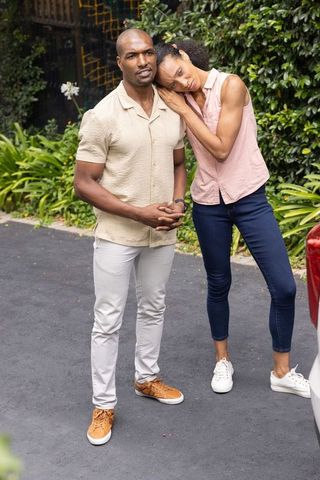 Diverse couple standing on driveway, woman leaning on partner's shoulder, tender moment