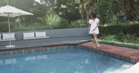 African american woman walking barefoot on brick pool edge in white dress backyard oasis