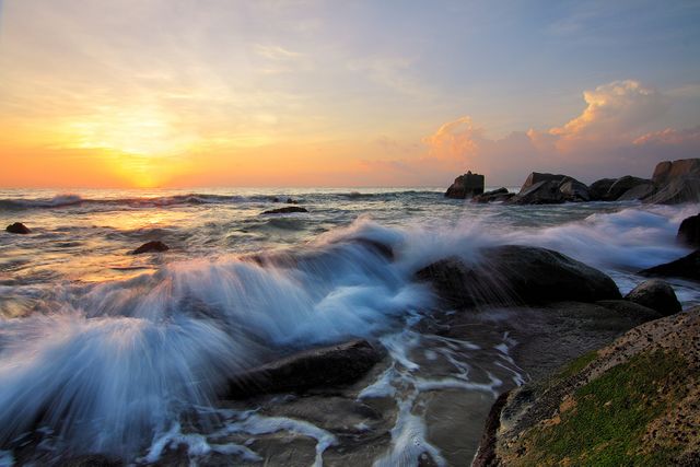 This beautiful scene captures waves crashing onto a rocky shoreline during sunset. Perfect for use in nature and travel websites, advertisements for coastal destinations, and desktop wallpapers depicting serene and natural beauty. Ideal for prompting relaxation and tranquility.