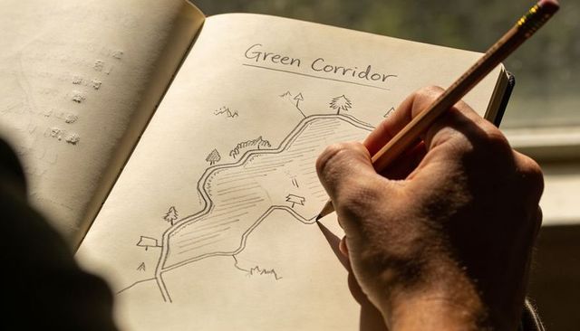 Hand sketching green corridor plan in sunlit notebook for urban design