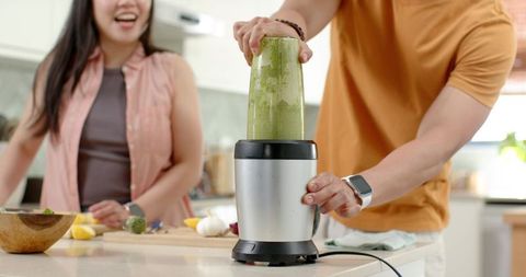 Asian couple preparing green smoothie with personal blender on modern kitchen island