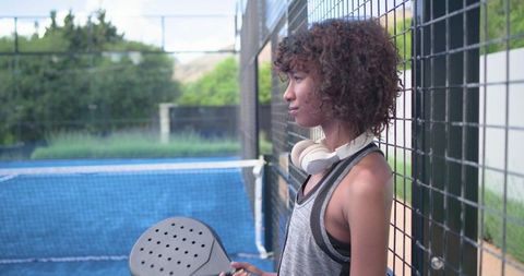 African american woman practicing pickleball wearing headphones on blue outdoor court
