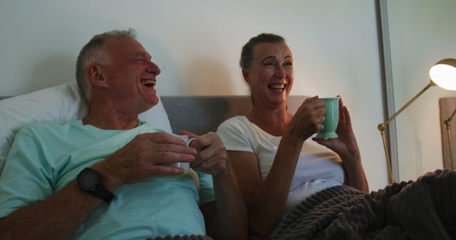 Caucasian senior couple laughing while drinking coffee cup in bed at home. staying at home in self isolation in quarantine lockdown