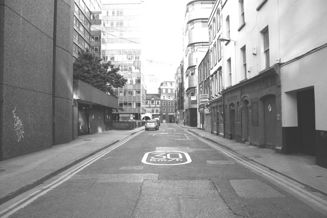 Urban street with speed limit marking, showing empty road flanked by buildings. Useful for topics on urban life, city planning, infrastructure, travel, and transport. Depicts a calm moment in a busy city setting, highlighting the contrast between architecture and empty space.