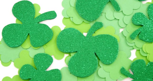 Green shamrock cutouts, some with glitter, are scattered across a white background, symbolizing St. Patrick's Day celebrations. These decorations evoke the spirit of the Irish holiday, often associated with luck and festivity.