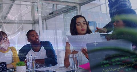 Team analyzing financial data and charts in glass conference room with digital overlays