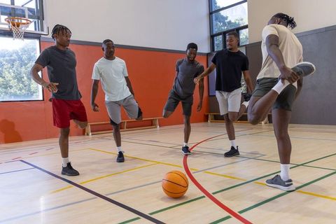 African american men stretching and balancing on indoor basketball court warming up