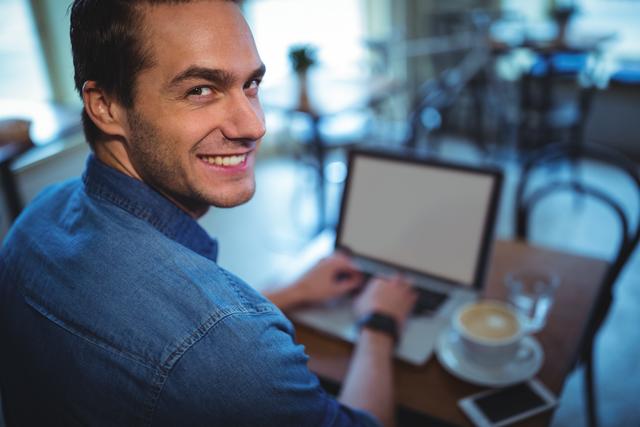 Portrait of man using laptop while having coffee in cafÃ©