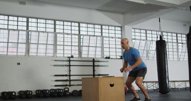 Man performing box jumps in fitness center. Ideal for illustrating workout routines, healthy lifestyles, fitness blogs, and exercise demonstrations focused on strength and agility training.