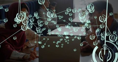 Woman wearing hijab pointing and explaining with colleagues around laptop showing holographic networ
