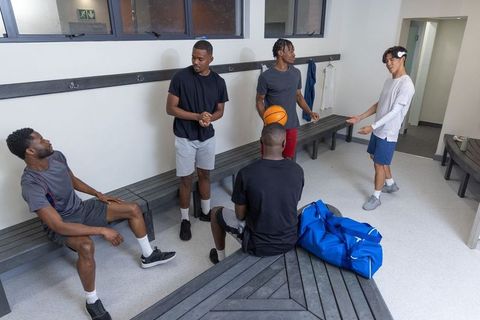 Locker room teammates chatting and laughing holding basketball and duffel bag, team bonding