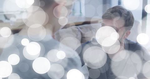 Mid-adult man talking with boy on sofa amid soft bokeh lights in calm home interior