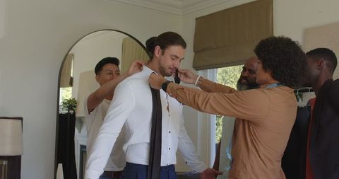 Friends helping groom with tie on wedding day preparation