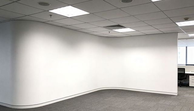 Curving white partition wall defining modern open-plan office with desk and natural light