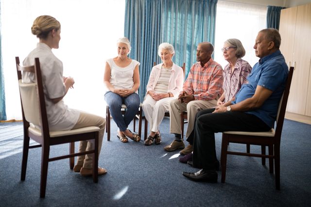 Female doctor sitting with senior people on chairs against window at retirement home