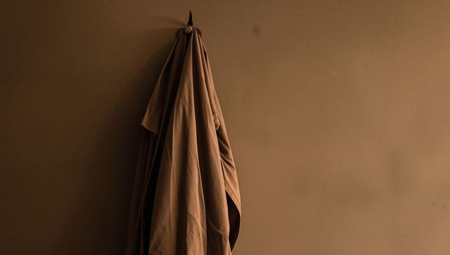 Hanging brown garment with deep vertical folds on warm wall minimal textile still life