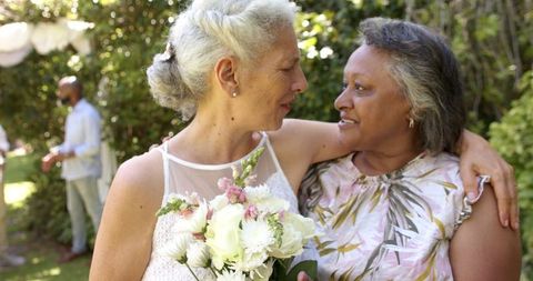 Senior Bride and Bridesmaid Embrace at Joyful Outdoor Wedding