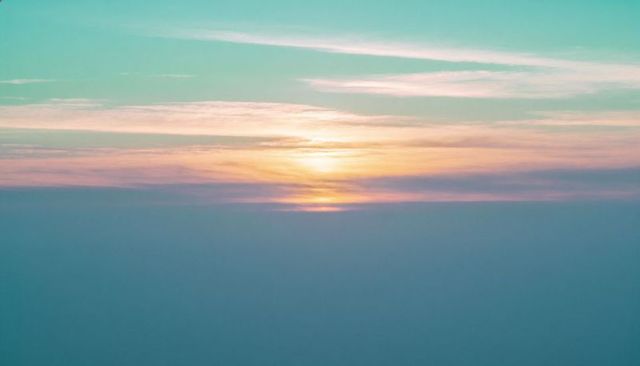 Glowing sunrise above cloud deck with pastel sky, cirrus streaks, soft fog, serene horizon