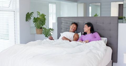 Couple Relaxing in Bright Modern Bedroom on King Bed Chatting and Laughing with Greenery