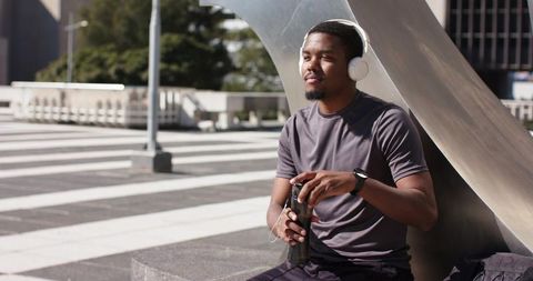 African american man listening to music on headphones while resting on urban plaza ledge