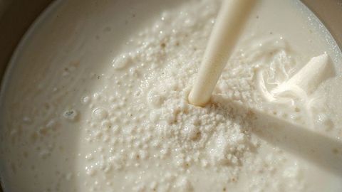 Pouring frothy cream into latte coffee cup creating bubbles