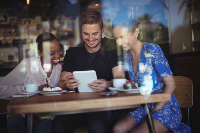 Happy friends using digital tablet while having breakfast in restaurant