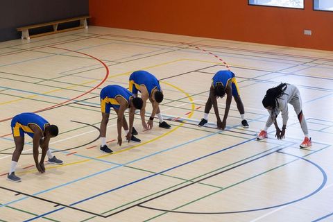 Basketball Players and Coach Stretching on Indoor Court
