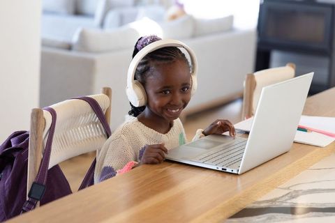 African american girl smiling, using laptop and headphones at home counter