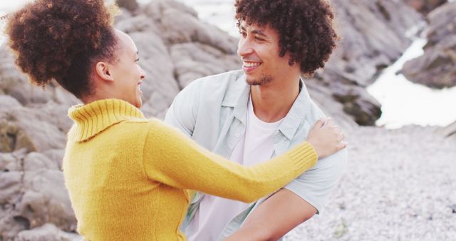 Couple embracing and smiling at a rocky beach during the daytime. Ideal for themes around love, romance, leisure time, nature, and happiness. Useful for advertisements, social media campaigns related to relationships, travel brochures, and lifestyle blogs.