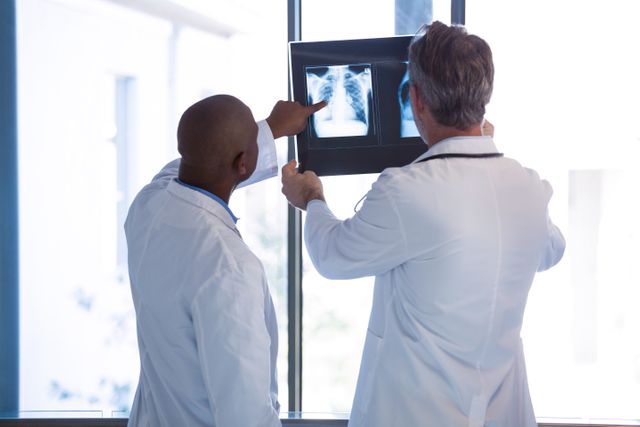 Doctors analyzing an x-ray report in a hospital corridor. Ideal for use in healthcare, medical, and hospital-related content. Can be used for articles, blogs, and presentations about medical diagnosis, teamwork in healthcare, and radiology.