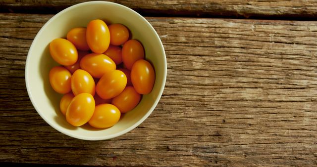 Bowl filled with fresh yellow cherry tomatoes on rustic wooden table. Perfect for illustrating healthy eating, organic lifestyle, farmers market produce, and vegan diet. Useful for blogs, websites, and magazines focused on healthy recipes, nutrition, and culinary preparation.