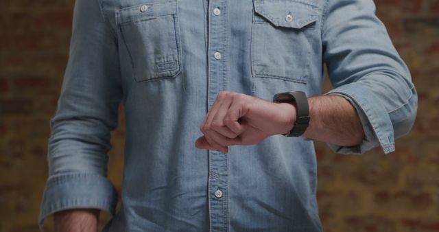 Man in denim shirt checking time on smartwatch. Modern lifestyle combined with casual fashion, making it suitable for promoting tech gadgets, smartwatches, lifestyle blogs, time management articles, or any advertisement related to fashion and technology integration.