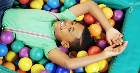 Joyful boy relaxing in colorful ball pit