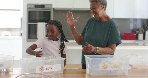 African american grandmother and granddaughter sorting recyclables in bright modern kitchen