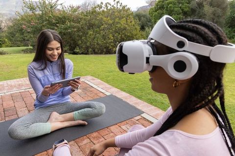 Diverse friends practicing outdoor wellness with vr headset and tablet on yoga mats