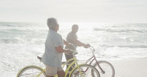 Senior Couple with Bicycles Enjoys Beach Walk During Sunset