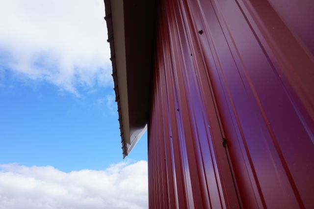 Close-up view of a red barn exterior against a blue sky with scattered clouds, showcasing rural architecture and agrarian life. Useful for illustrating themes related to farming, the countryside, and pastoral settings, as well as for backgrounds in agricultural and rustic visual presentations.