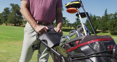 Senior golfer transporting golf clubs across lush course