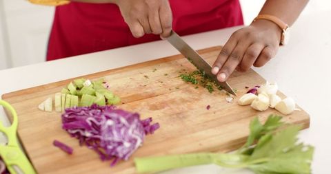 Woman Chopping Fresh Herbs with Vegetables on Kitchen Board
