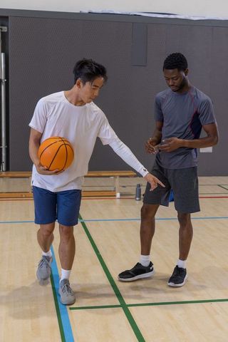 Asian and african american teammates practicing basketball footwork drills on gym court