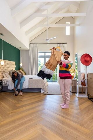 Friends choosing dress in bright modern bedroom with vaulted ceiling and herringbone floor